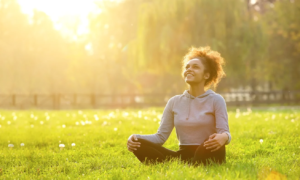 a woman sits cross-legged on grass, the sun is bright behind her
