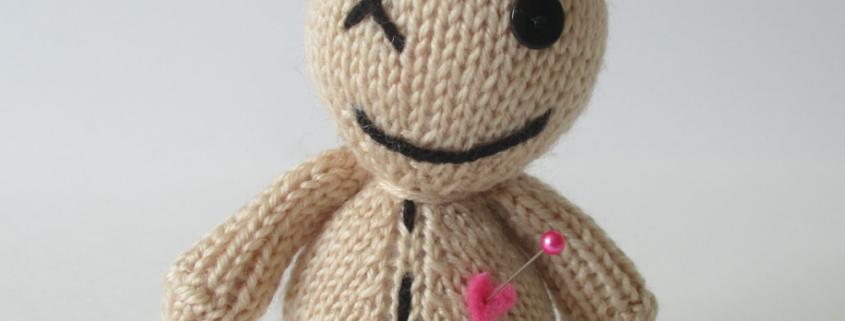 A picture of a cute hand knit voodoo doll, with pins in its head