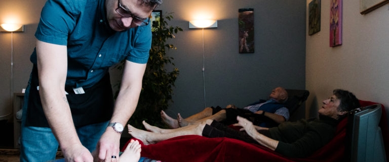 Several people relaxing after receiving acupuncture. Acupuncturist removes needles from a patient in the foreground
